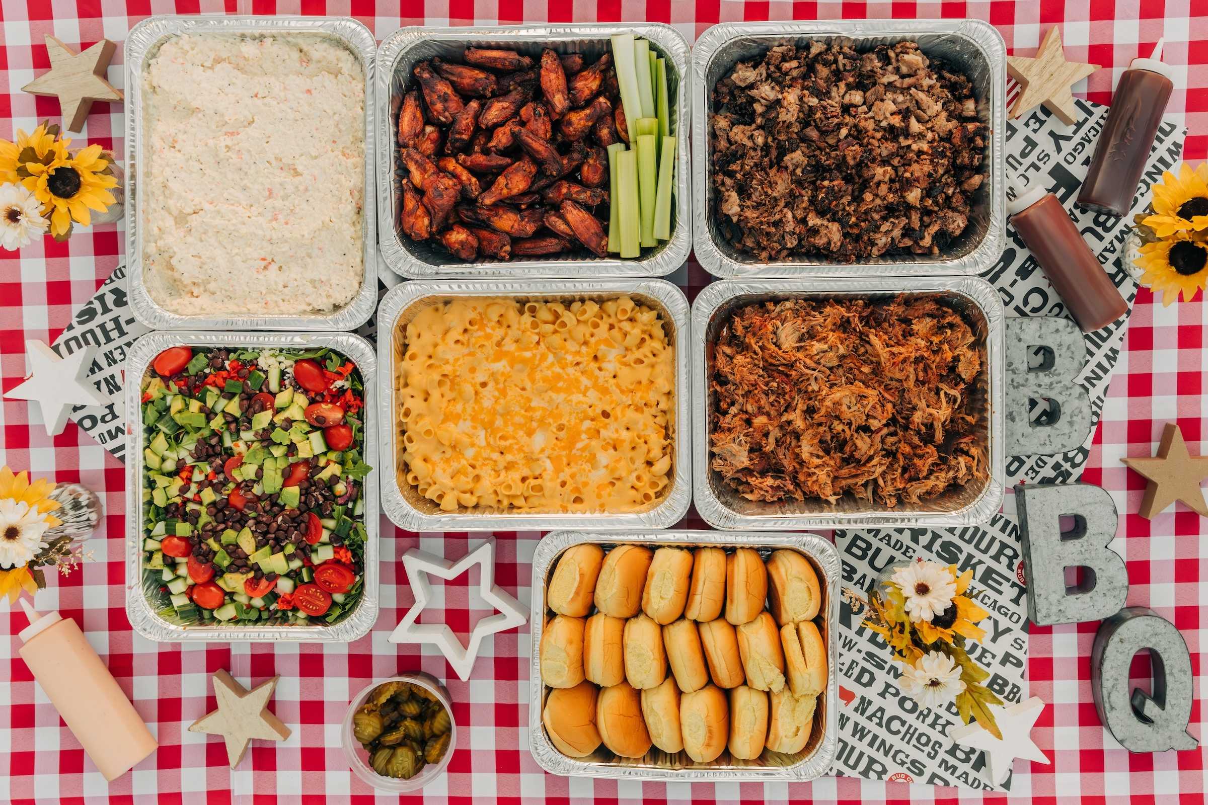 Spread of catering platters such as wings, mac n' cheese, salad, and smoked meats.